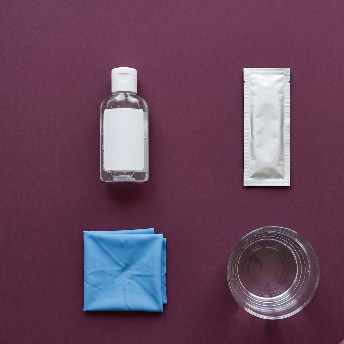 Flatlay mit Gleitgel, Lecktuch, Kondom und Wasserglas auf pflaumenfarbenem Grund