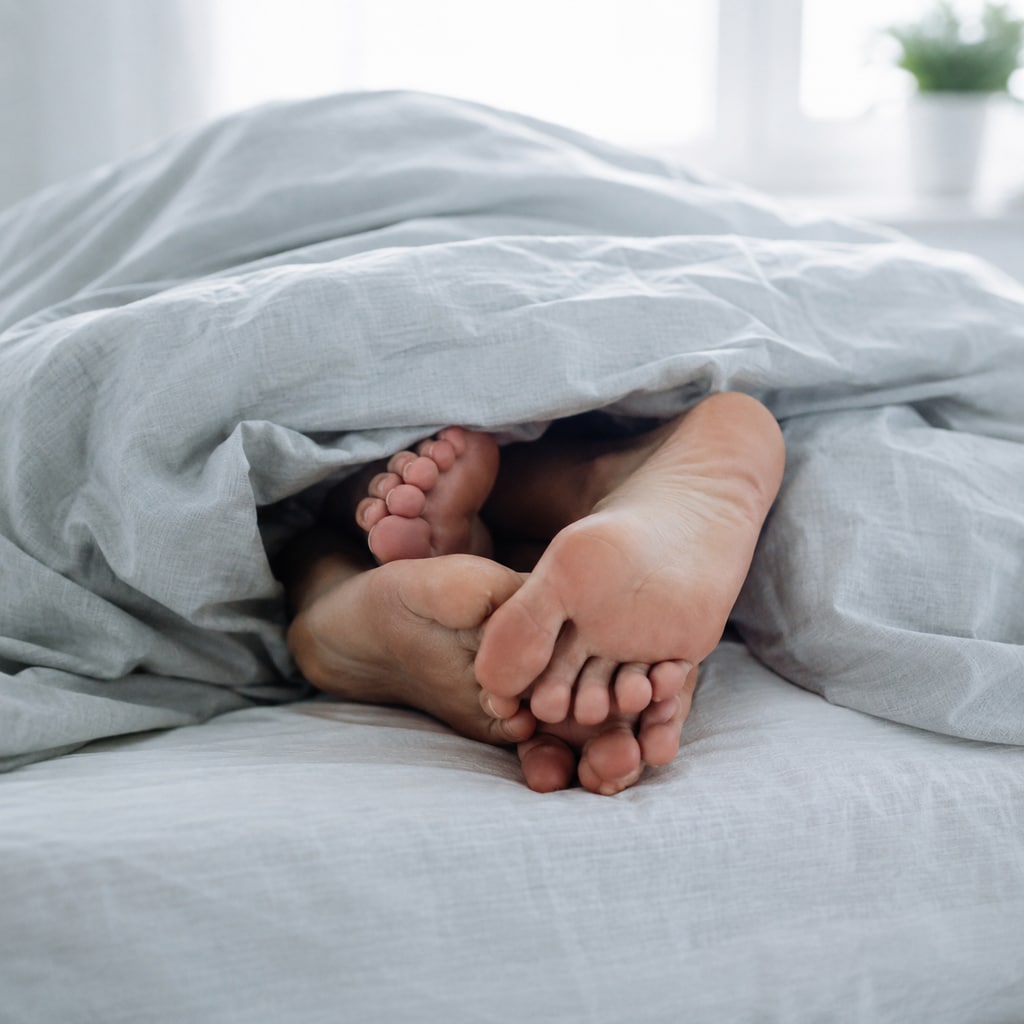 Zwei nackte Füße unter einer hellen Leinendecke, ineinander verschlungen